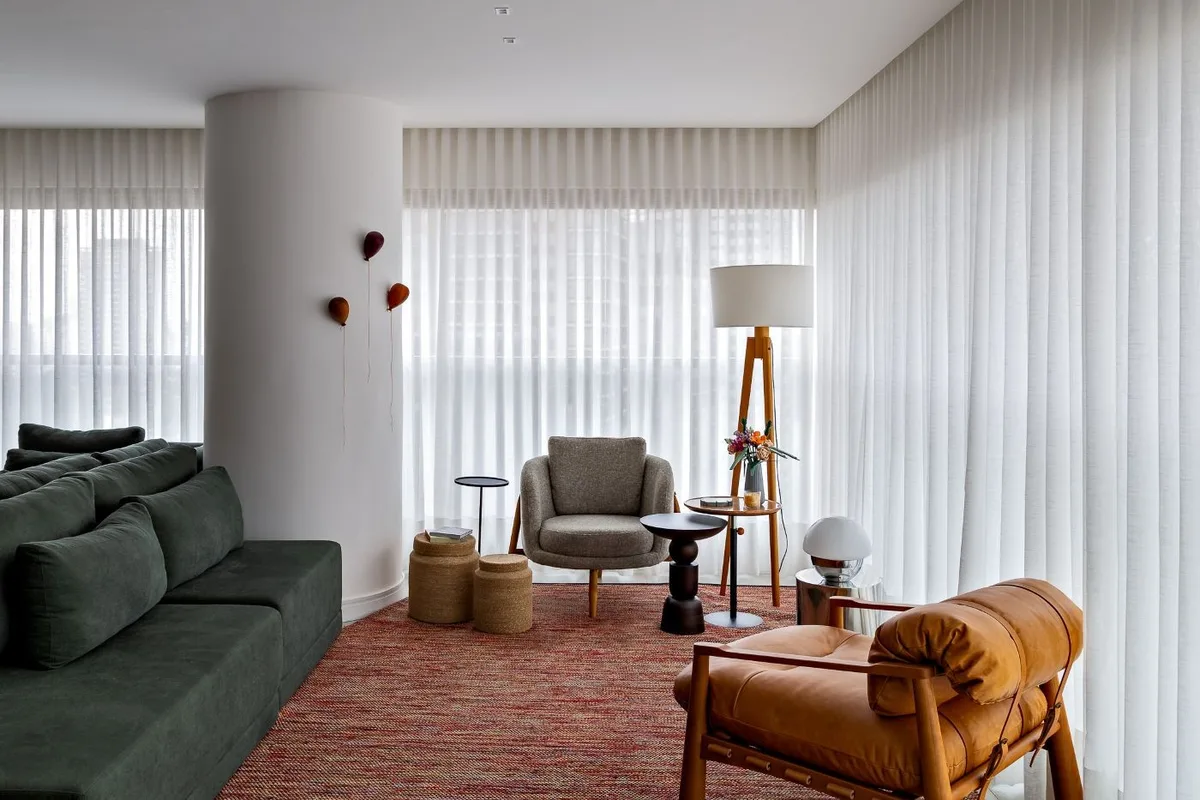 Apartamento em São Paulo integra living com sofá verde ao redor de pilar